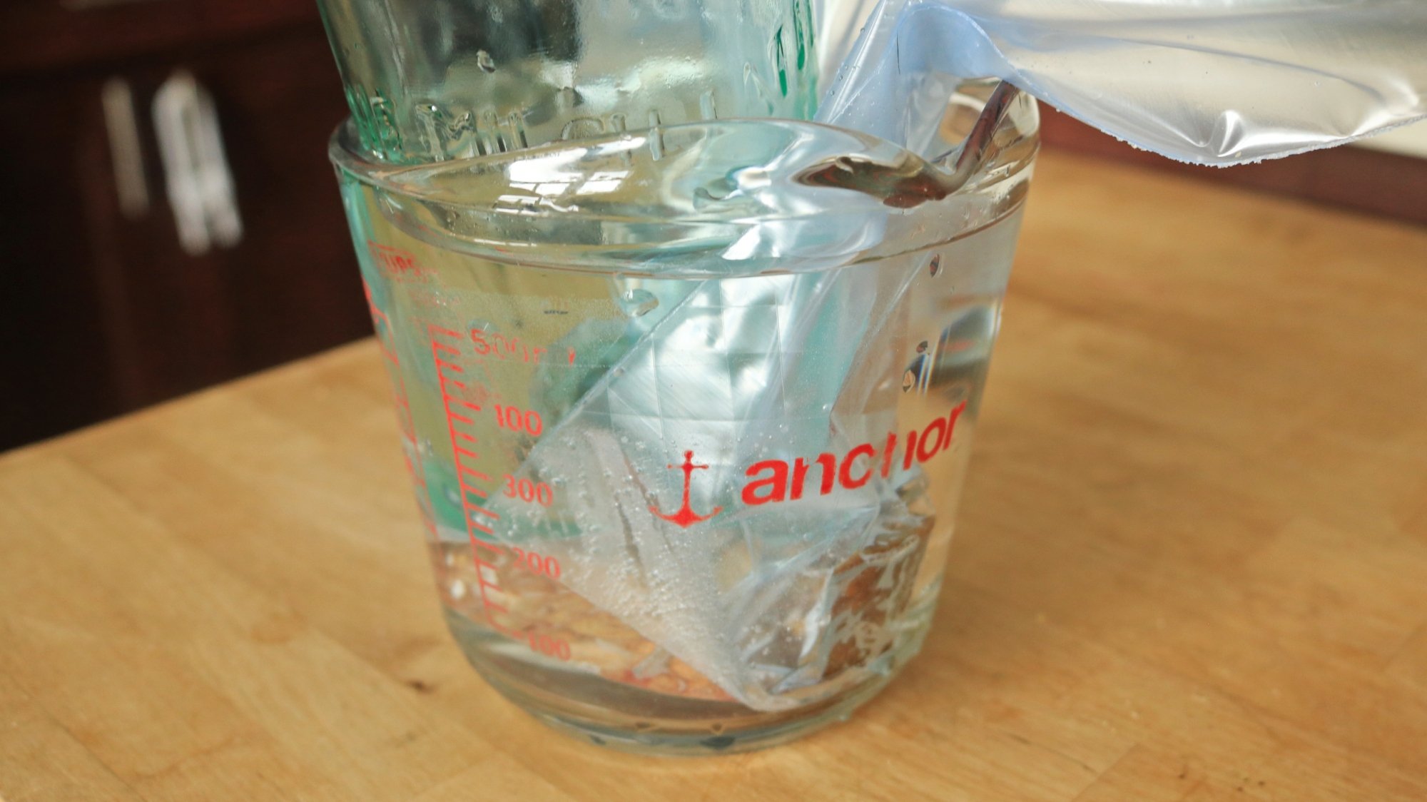 A steak in a zip-top bag submerged in water inside of a measuring cup.