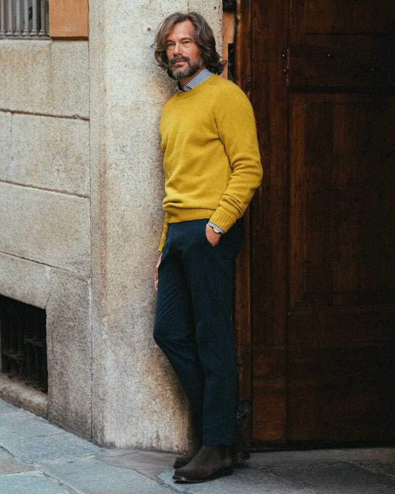 man in a yellow sweater leaning to a wall of a building